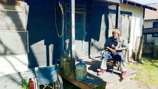 A resident of Sandbranch sits on his porch with water jugs nearby.Strategic Vision and Plan for Improvements to the Sandbranch Community